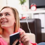 młoda blond kobieta siedzieć na kanapie trzymać smartfona w ręce