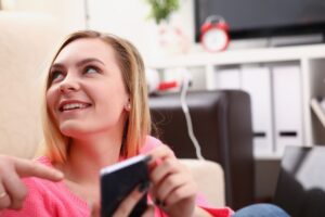 młoda blond kobieta siedzieć na kanapie trzymać smartfona w ręce