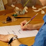 kobieca dłoń pisze atramentowym piórem słowa „dziękuję” i kaligrafia na białej kartce papieru z papeterią w paski na biurku z bliska widok z góry lekcje ortografii i ćwiczenia kaligrafii