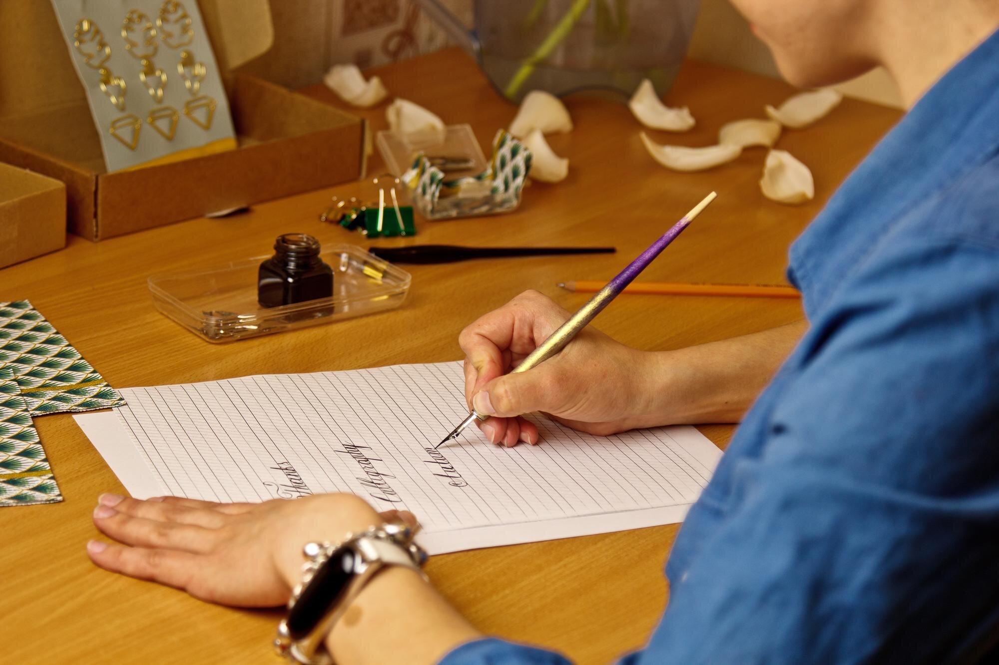 kobieca dłoń pisze atramentowym piórem słowa „dziękuję” i kaligrafia na białej kartce papieru z papeterią w paski na biurku z bliska widok z góry lekcje ortografii i ćwiczenia kaligrafii