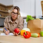 Kobieta w średnim wieku w okularach zapisuje wydatki na zakupione jedzenie