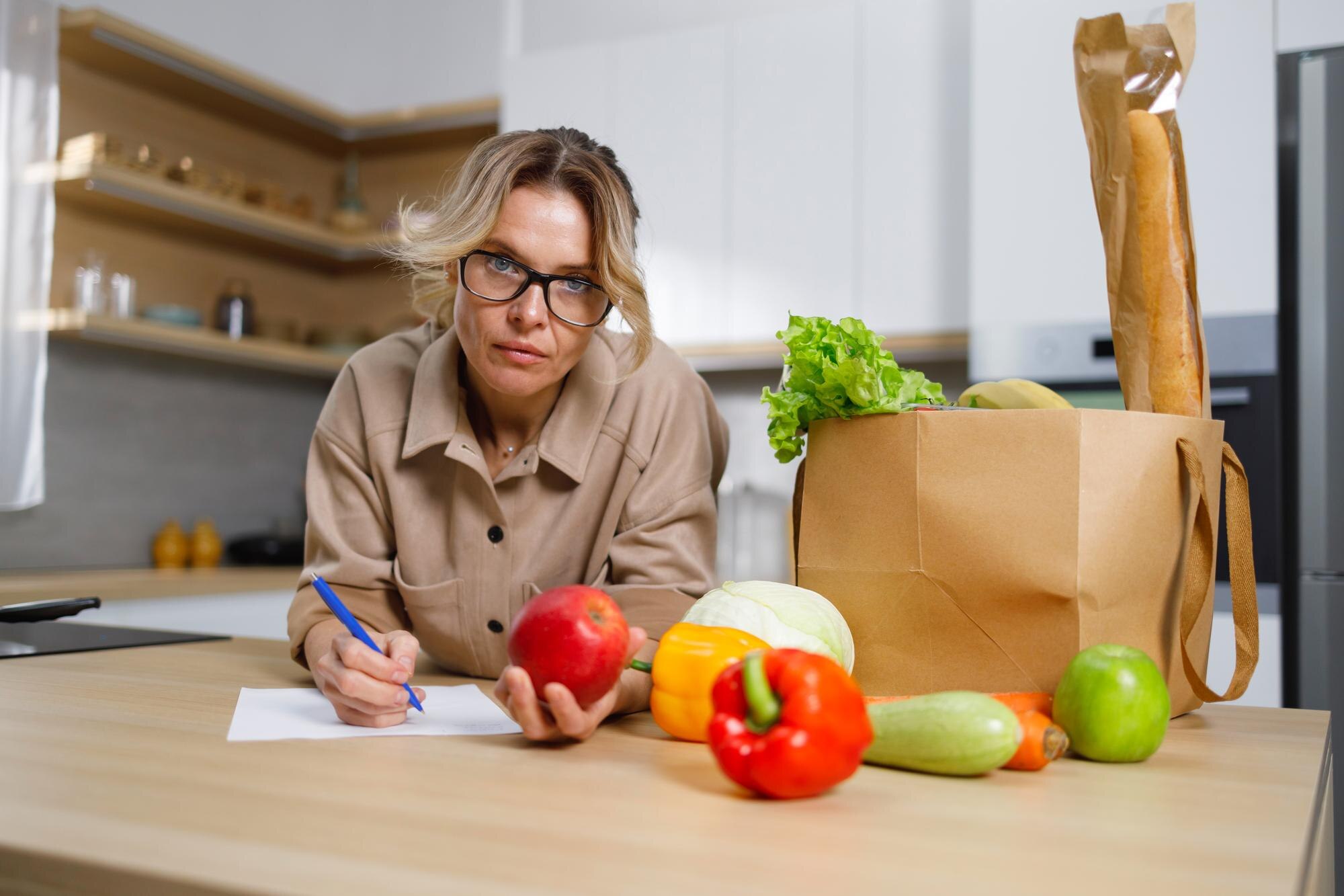 Kobieta w średnim wieku w okularach zapisuje wydatki na zakupione jedzenie