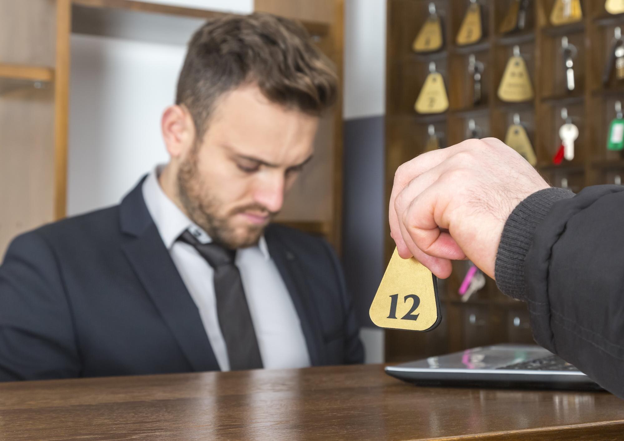 Odcięta ręka mężczyzny dająca klucz do concierge'a na recepcji hotelu